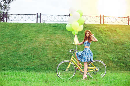 Outdoor fashion portrait of elegant lady riding her hipster retro bike in stylish skirt. Enjoy summer day, posing on the green lawn.の写真素材