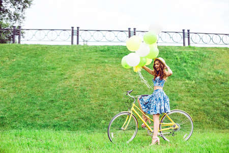 Outdoor fashion portrait of elegant lady riding her hipster retro bike in stylish skirt. Enjoy summer day, posing on the green lawn.の写真素材
