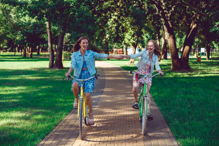 Female friends enjoying cycling on a summer day, holding hands. Two young female friends riding their bicycles on a summer day in park.の写真素材