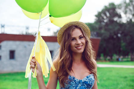 Portrait of a beautiful smiling woman in a straw hat holding balloons. A girl is resting on a sunny day in the park.の写真素材