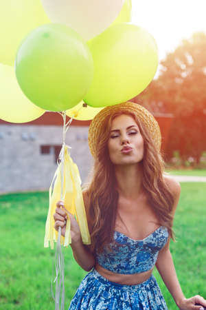 Portrait pretty woman making air kiss with green and yellow balloons. Enjoy summer day, posing on the green lawn.の写真素材