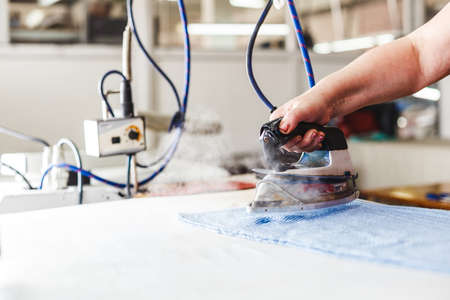 Close up of professional iron in a tailors factory. Woman hand ironing in store or fabric.の写真素材