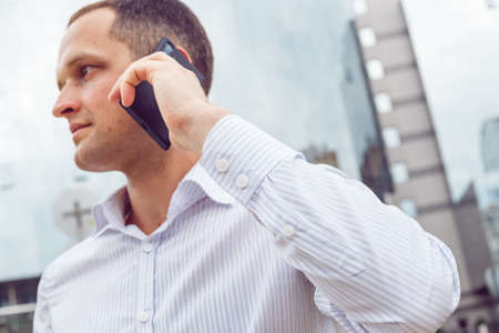 Close up portrait of serious businessman talking on mobile phone. Young businessman with cell phone near business centerの写真素材