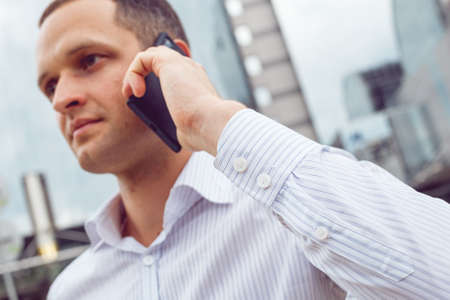Close up portrait of serious businessman talking on mobile phone. Young businessman with cell phone near business centerの写真素材
