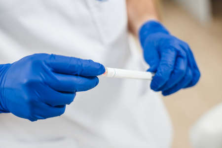 Close up view of DNA swab of saliva in doctors hands. Mens hands in blue gloves hold DNA swab of saliva.の写真素材