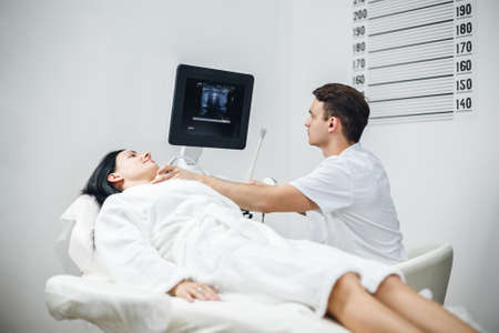 Beautiful woman doing neck ultrasound examination at hospital. Handsome man doctor onducts examination of the patient.の写真素材