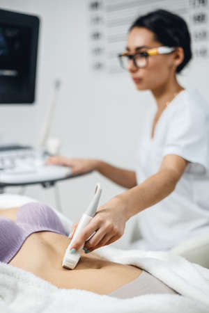 Doctor makes the patient women abdominal ultrasound. Ultrasound Scanner in the hands of a doctor. Diagnostics and sonography in clinic.の写真素材