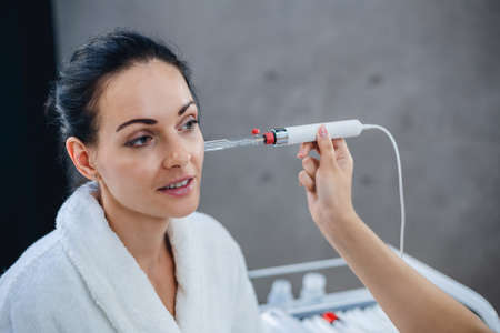 Doctor cosmetologist conducts diagnostics of a condition of a skin of the face of the patient. Picture of nice beautician doing beauty therapy for young womanの写真素材