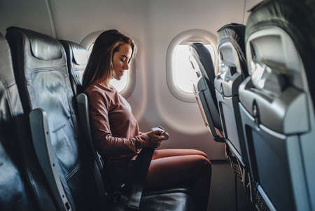 Girl is strapped on the plane near windowの写真素材