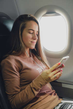 Girl is reading from smartphone in airplane near windowの写真素材