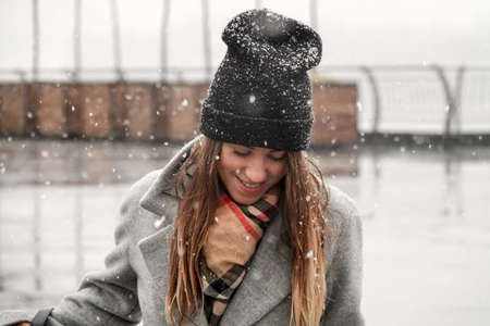 Portrait of a girl in a hat and a gray coat. A young woman is walking in the snow in the city.の写真素材