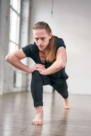 Young fit man stretching legs doing forward lunge. Handsome ballet dancer training in the gym.の写真素材