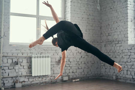 The young attractive modern ballet dancer in black jacket jumping over urban background.の写真素材