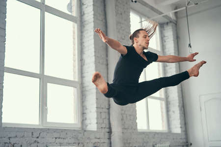 The young attractive modern ballet dancer in black jacket jumping over urban background.の写真素材
