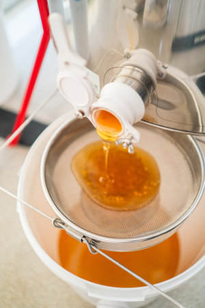 Honey Flowing out of the Centrifugal Honey Extractor Barrel to be FIltered with a Sieve