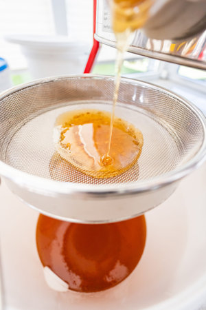 Smooth and Creamy Golden Honey Flowing Into the Filtration Sieve