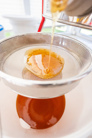 Golden Honey Flowing Into the Filtration Sieve Smoothly