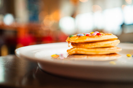 Drop of Honey Dripping Down a Stack of Pancakes with Colorful Topping Chocolate Lentilsの写真素材