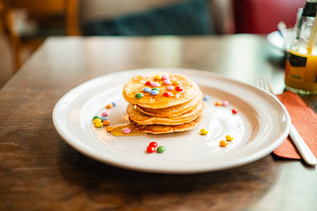 Breakfast Plate with Small Stack of Pancakes Topped with Colorful Chocolate Lentilse and Honeyの写真素材