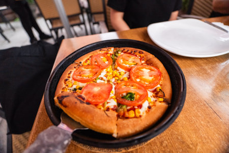Vegetarian Broccoli Pizza in a Frying Pan With Cheese and a Baked Crust Picking a Pizza Slice from the Pan in a Restaurantの写真素材