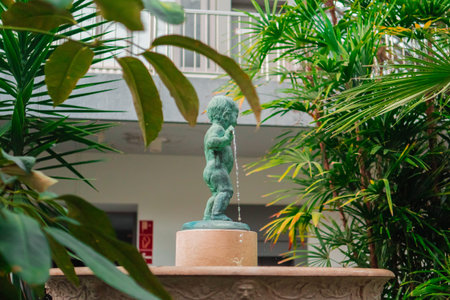 Water Fountain With Green Oxidized Bronze Statue Surrounded by Plantsの写真素材