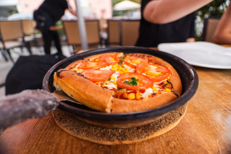 Picking a Slice of Vegetarian Tomato Pizza From a Frying Pan Topped With Tomatoes Corn Cheese and Surrounded by a Brown Baked Crusty Crustの写真素材