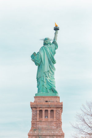 Statue of Liberty from behind looking into the sky of clouds representing its landmark statue in New York Cityの写真素材