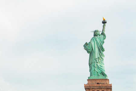 Statue of Liberty from behind looking into the sky of clouds representing its landmark statue in New York Cityの写真素材