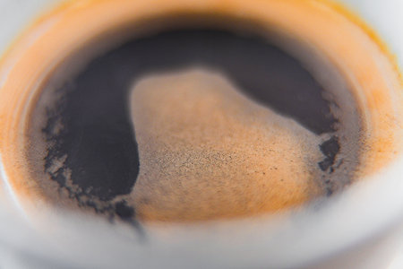Extreme Close-Up of a Dark Black Coffee with a Little Foam on Top in a White Coffe Mug on a White Plate Showing the Foam in Detailed Perspective within the Mugの写真素材