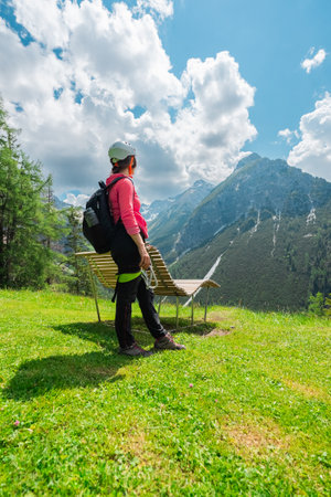 Woman Sport Climber with Helmet Standing on a Green Lawn Ready for Adventure Looking up the Mountain Landscapeの写真素材