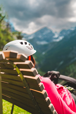Climber with Helmet Resting on a Wooden Bench in a Mountain Landscapeの写真素材