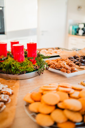 Christmas Bakery with Tasty Macroons Biscuites and Choclate Covered and Decorated Cookies on the Kitchen Table Top Near an Advent Wreath with Red Candlesの写真素材