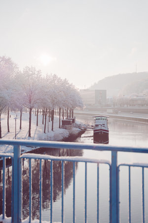 Calm River with a Boat Near a Snow Covered Park Avenue on a Cold Hazy Sunny Winter Dayの写真素材