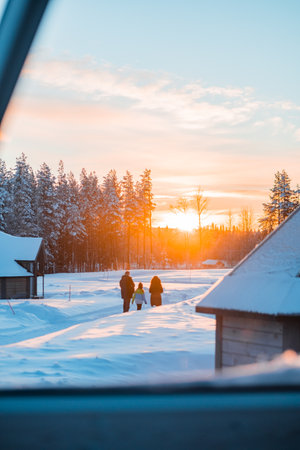 Family of Three Walking Through the Snow Against the Sunlight in a Snow Covered Forest Environmentの写真素材