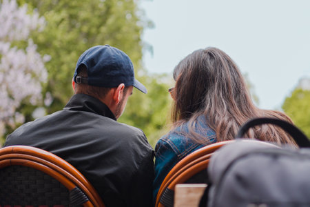 A Man and a Woman as Couple Sitting Together on Chairs Outdoors in the Park Showing their Backsの写真素材
