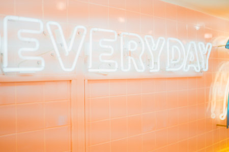 Everyday Neon Light Lable Shining in Bright Hazy Light on a Beige Pink Tile Wallの写真素材