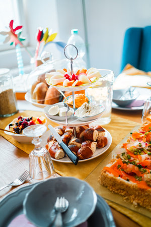 A perfectly arranged breakfast spread featuring a fruit platter, pastries, and pretzels on dining table lit by bright sunlight. Perfect for gatherings or a leisurely morning meal.の写真素材