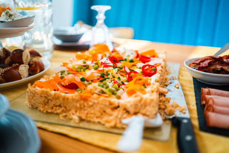 A vibrant vegetable tart garnished with fresh vegetables alongside a selection of meats and breads, beautifully arranged on a breakfast table, creating an inviting and appetizing dining atmosphere.の写真素材