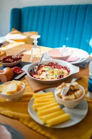 A bright and inviting breakfast table featuring warm shakshuka, assorted cheeses, and meats, creating a cozy and welcoming dining experience.の写真素材