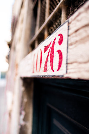 A close-up image of a building address sign featuring red numbers. The focus is on the textured details, reflecting the rustic architectural charm of a European street, likely in Venice.の写真素材