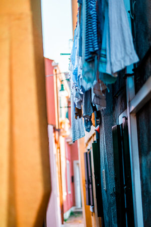 Capture of a narrow Venetian alleyway with laundry hanging from colorful buildings. The ambient light adds warmth to this picturesque Italian street scene.の写真素材