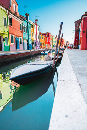 Picturesque canal in Burano, Venice features vibrant, colorful buildings and traditional boats. The bright architecture reflects in the calm water, showing the charm of this Italian townの写真素材