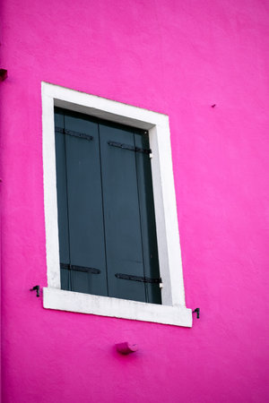 A striking contrast between a vivid pink wall and closed dark green shutters highlights the artistic essence of Venice. The minimalist, colorful architecture evokes creativity and bold design.の写真素材
