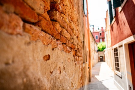 Close view of a rustic brick wall in a sunlit alleyway in Venice, Italy, capturing the historic charm and texture of the architecture.の写真素材