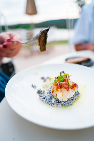 An elegant seafood dish served on a white plate, showcasing gourmet dining outdoors. A blurred...
