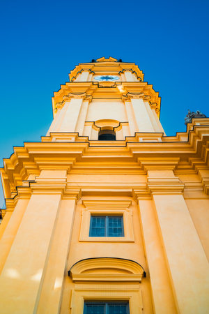 Stunning architectural details of a historical clock tower in Munich, showcasing intricate designs against a striking blue sky. The sunlit yellow facade adds warmth to this iconic structureの写真素材
