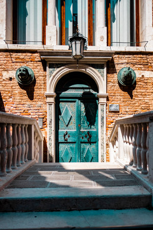 A vintage green door set within a historic Venetian building showcases rich brickwork and architectural detail in warm sunlight, reflecting the charm and elegance of Italy's timeless design.の写真素材