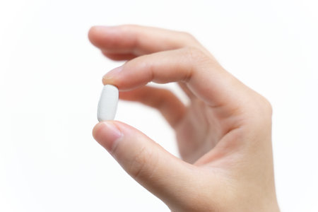 Female hand holding a white pill on a white background. Close up.の写真素材
