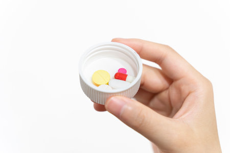 Hand holding pill bottle isolated on white background. Focus on foreground.の写真素材