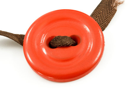  	 Old red button with a brown ribbon on a white background 